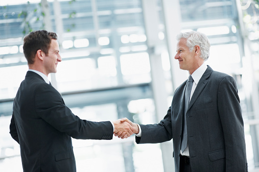 Handshake of two businessmen on the background of empty modern office, partnership concept, close up
