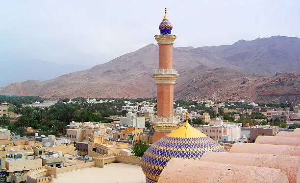 Skyline of Nizwa in central Oman.  The mountain, Jebel Akhdar, is visible in the background.  A mosque with single minaret is in the foreground.