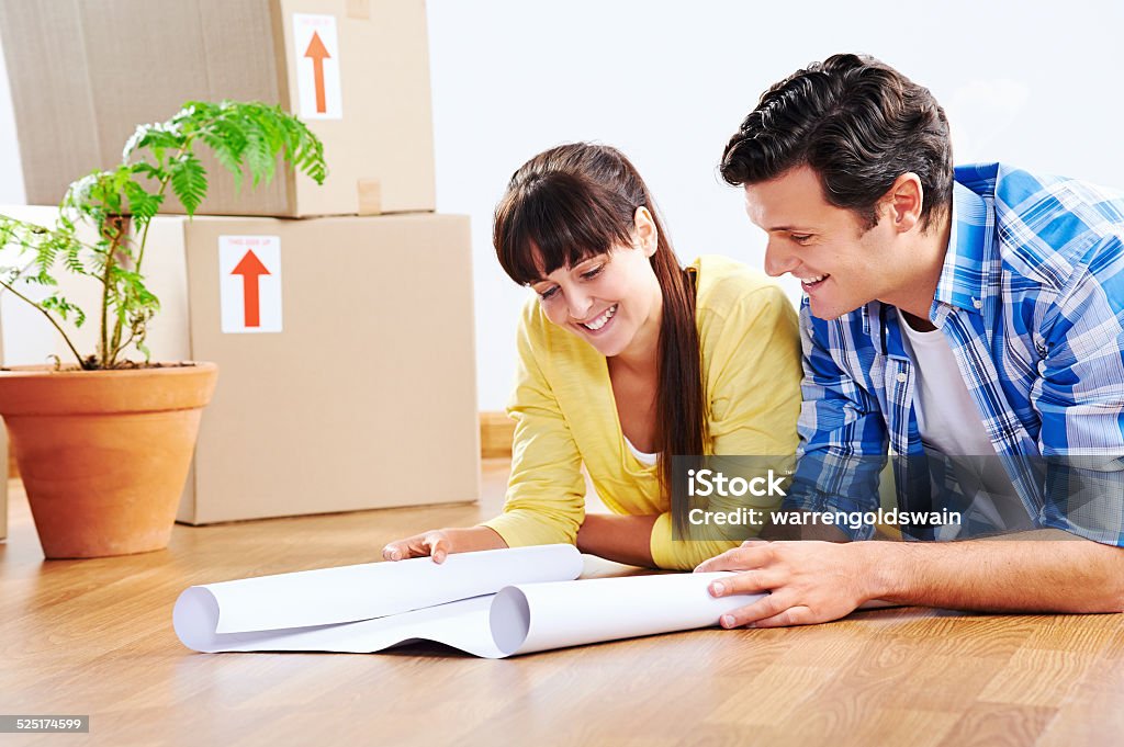new house plans couple looking over plans to new house together lying on wooden floor Activity Stock Photo