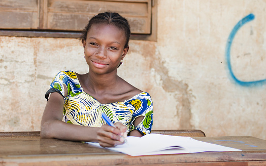 In Bamako (Mali), a young schoolgirl is concentrated while writing on her exercise book. She proudly smiles while looking at the camera.