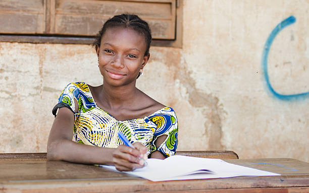 Back To School: African Teenage Girl Smiles in Public School In Bamako (Mali), a young schoolgirl is concentrated while writing on her exercise book. She proudly smiles while looking at the camera. Mali stock pictures, royalty-free photos & images