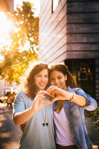 Best girl friends show heart shape to camera with hands