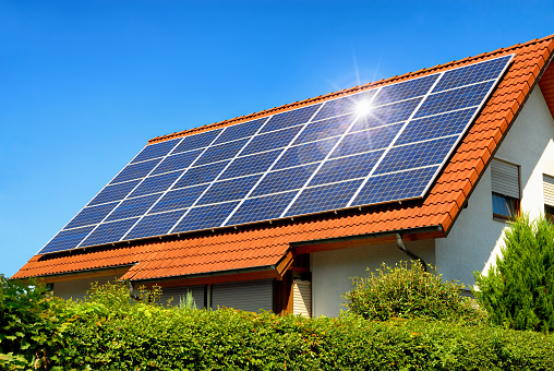 Solar panel on a red roof reflecting the sun and the cloudless blue sky