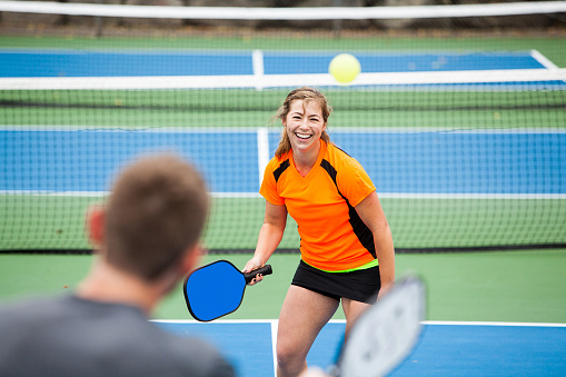Female Pickleball player is returning a serve on an outdoor court. 
