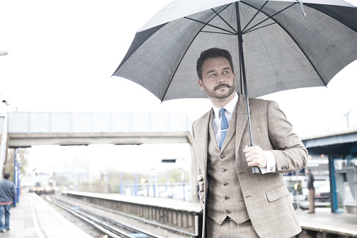 Young trendy businessman travelling to work in typical English Weather