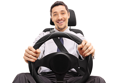 Cheerful guy holding a steering wheel seated on a car seat isolated on white background