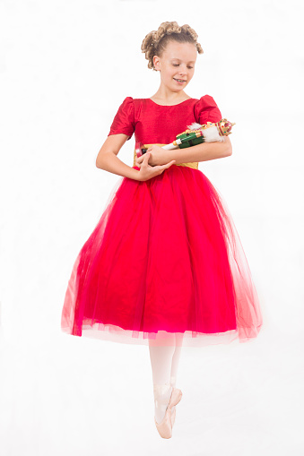 Caucasian girl with blond curls wearing a red party dress holds a nutcracker doll as she portrays Clara and is isolated against a white background
