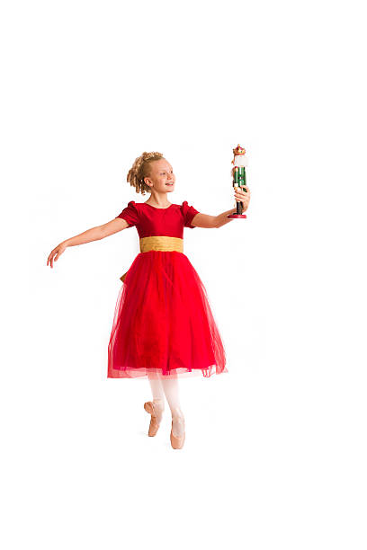 Clara from Christmas Nutcracker ballet Beautiful dainty Caucasian girl with blond curls wearing a red party dress portrays Clara from the Christmas Nutcracker ballet as she stands en pointe holding a nutcracker doll against a white background nutcracker photos stock pictures, royalty-free photos & images