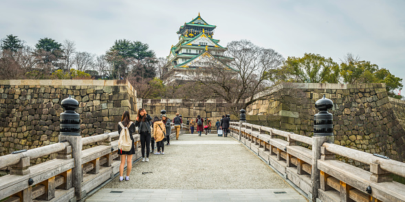 Osaka, Japan - February 23, 2016: Tourists on Gokurakubashi Bridge over the moat in Osaka Castle Park beneath the iconic five storey keep in the heart of Japan's vibrant second city. Panoramic image created from six contemporaneous sequential photographs. 