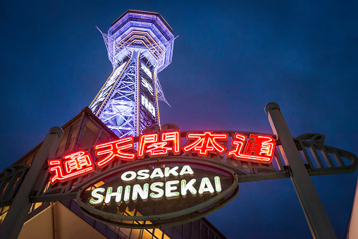 Osaka, Japan - February 23, 2016: The iconic spire of Tsutenkaku Tower illuminated against deep blue dusk skies overlooking the neon signs of Shinsekai in the heart of Osaka, Japan's vibrant second city.