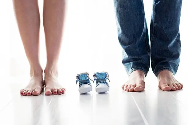 Future mom and dad feet with little baby shoes on the floor. Happy young family awaiting baby, love and happiness, new life concept