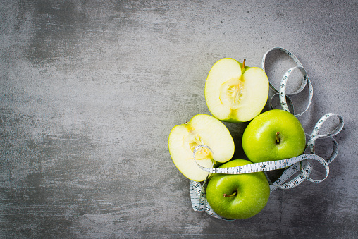 Green apples with measure tape on concrete background