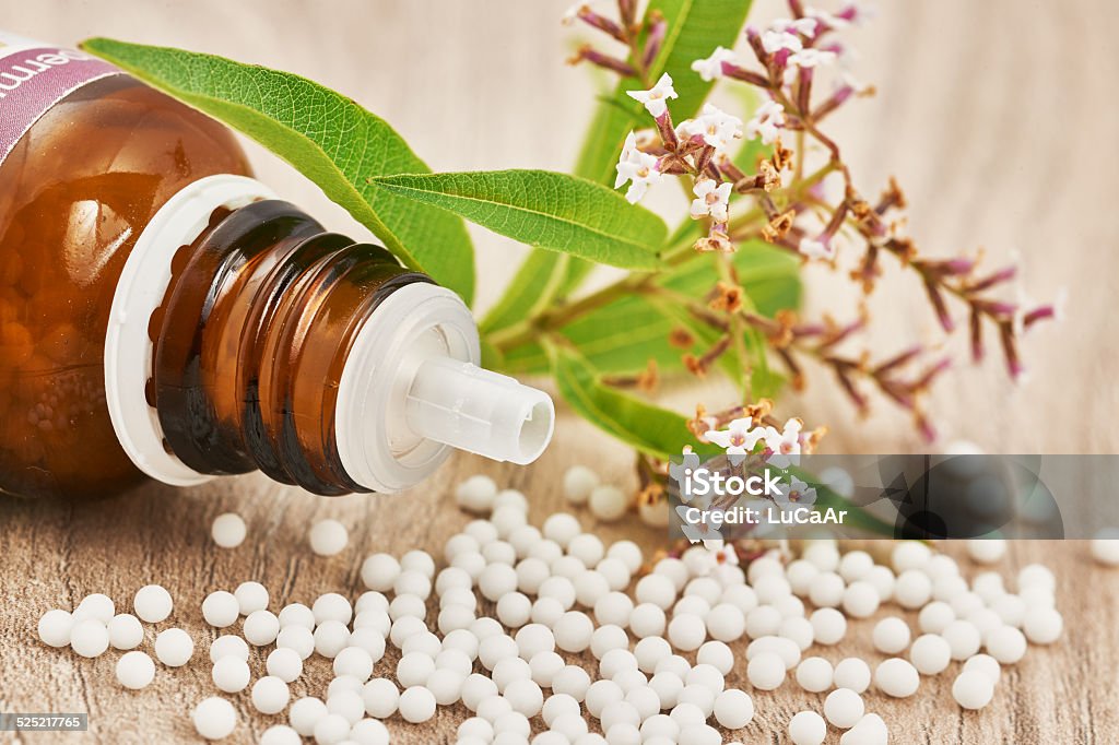 Homeopathic granules scattered on a wooden table Homeopathic granules scattered around a glass bottle and a medicinal herb on a wooden table Alternative Medicine Stock Photo