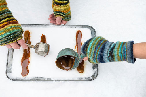 An unrecognizable man and child make maple syrup taffy by pouring boiled maple syrup in the snow to harden.  A northern American and French Canadian traditional candy made outdoors in the winter.  View from above.