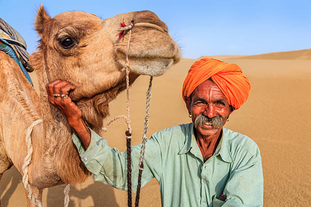 istock Indian man holding camel on sand dunes, Rajasthan, India 525225408