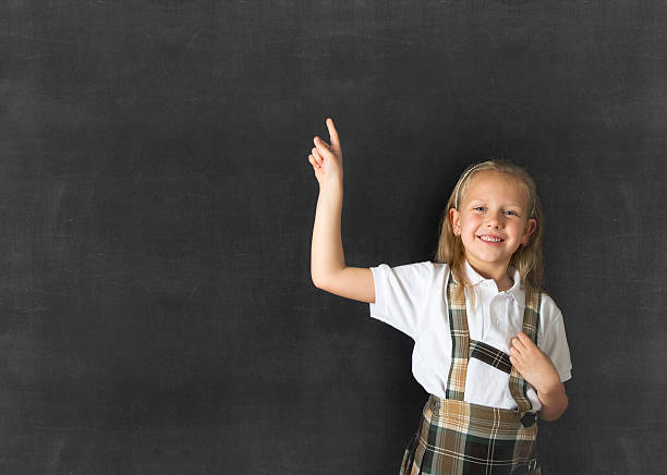 istock junior schoolgirl happy pointing to copy space on class blackboard 525227572