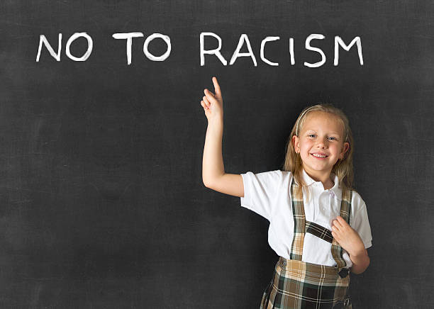 istock junior schoolgirl pointing text no to racism in classroom blackboard 525228018