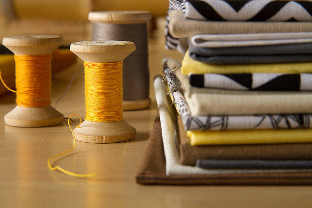 Modern patchwork fabrics in black, brown, white, yellow and grey on the wood table with yellow and grey sewing spools
