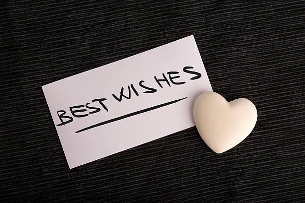 Best wishes for a loved one with a hand-written plain white card saying - Best Wishes - with a cream colored heart on a black background, overhead view.