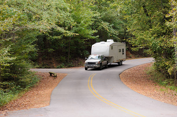 RV traveling down winding road Recreational vehicle fifth wheel travel trailer being towed down curving road in woods. RV truck stock pictures, royalty-free photos & images