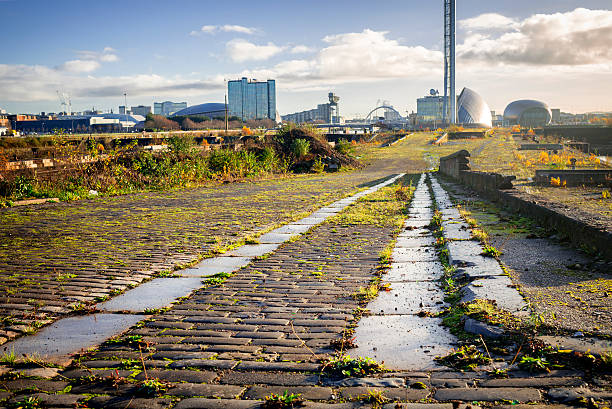 The Derelict Graving Docks at Govan, Glasgow Cobblestones and granite blocks amongst the overgrowth at the derelict Victorian graving docks - a type of dry dock - in Govan, Glasgow, on the River Clyde. In the background is the modern Glasgow skyline. govan stock pictures, royalty-free photos & images