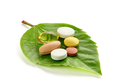 Kinds of vitamins and tablets on a green leaf isolated on a white background.