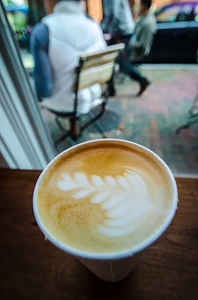 Vertical Cafe-latte cup of coffee sitting on table. Chairs and people in background. Barista art, leaf foam. Georgetown, Washington D.C.