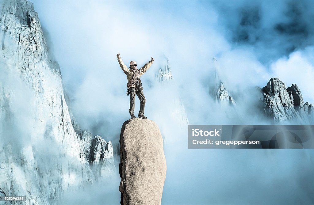 Climber on top of the mountain. Climber on the summit of a challenging cliff. Stunt Person Stock Photo