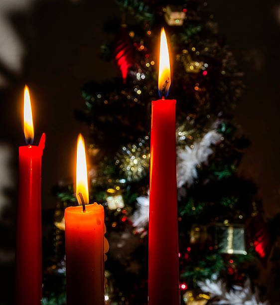 istock thhree candles glowing with christmas tree in background 525317215