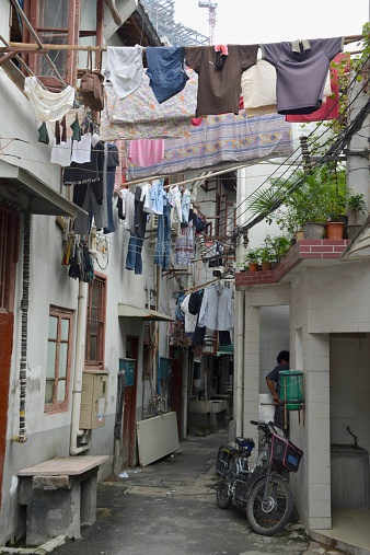 Shanghai, China - September 20, 2014: Man semi-covered behind a wall on a narrow street in Shanghai old City, surrounded by hanging drying clothes and sheets. China