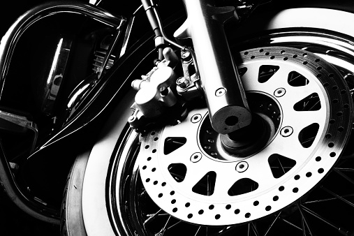 Brake disc on the front wheel of a cruiser motorcycle. Black and white studio image.