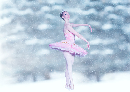 Smiling Caucasian ballerina dressed in a pink tutu dances in a winter wonderland