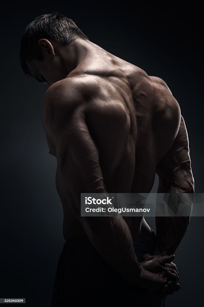 Men's Fitness Portrait of young, strong body builder on black background. Showing development of his back muscles 20-29 Years Stock Photo