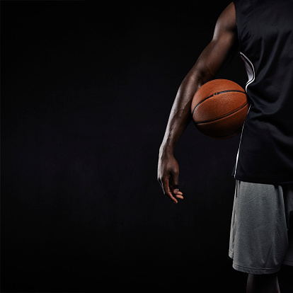 Cropped image of black basketball player standing with a basket ball. Man in sportswear holding basketball with copyspace on black background.
