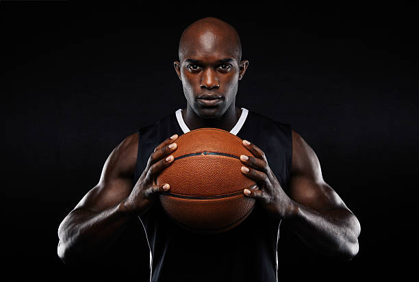 Afro american male basketball player with a ball Portrait of afro american male basketball player with a ball over black background. Fit young man in sportswear holding basketball. basketball sport stock pictures, royalty-free photos & images