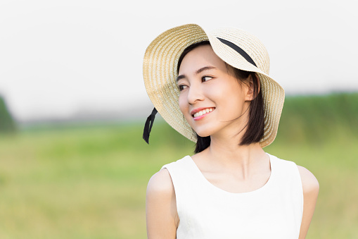 chinese girl wearing a white dress, standing on the green lawn, she took a sun hat