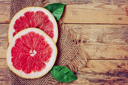 Two slices ripe grapefruit with leaves lie on canvas doily, rustic wooden table