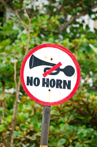 red, black and white road sign saying - no horn, India