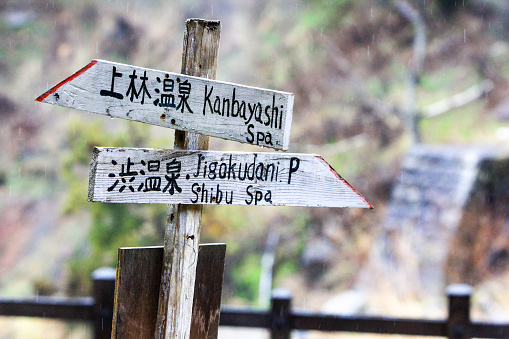 Yamanouchi, Japan - April 7, 2016: Steam from hot springs rises around a sign in Yamanouchi advertising the directions for Kanbayashi spa and the Jigokudani Monkey Park (home to the famous snow monkeys), both in the Nagano Prefecture. 