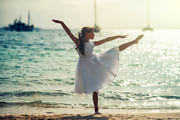 Little girl dancing ballet on the beach on sunny summer day. The ballerina is aged 9 and is is wearing white dress.