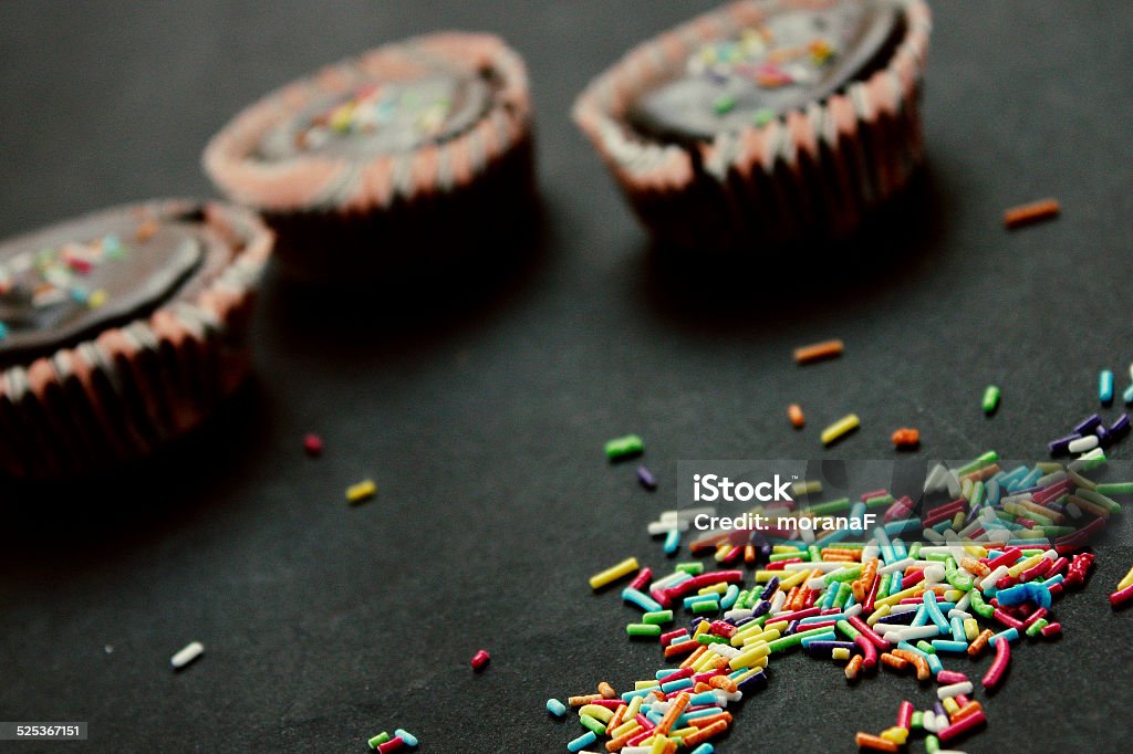 Rainbow sprinkles Rainbow sprinkles and muffins on dark background. Baking Stock Photo