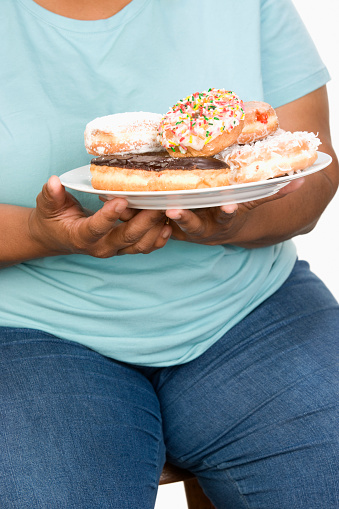 Mid-adult overweight  woman holding plate with donuts.