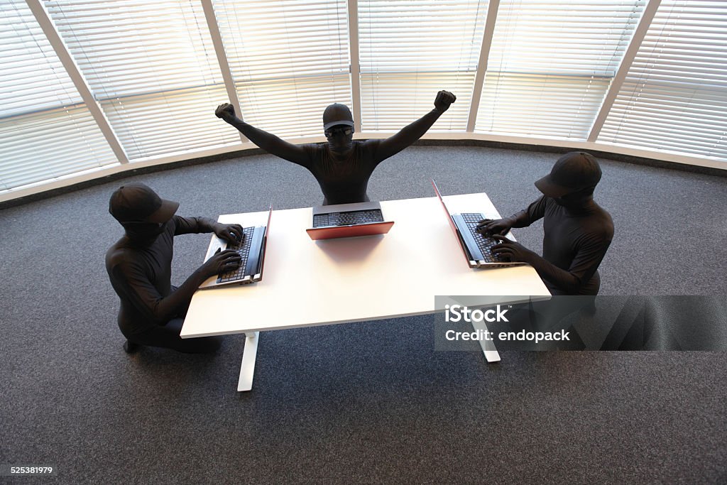 group of anonyous hackers working with computers in offic Log On Stock Photo