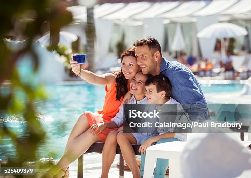 istock Family with two children taking selfie by resort swimming pool 525409379