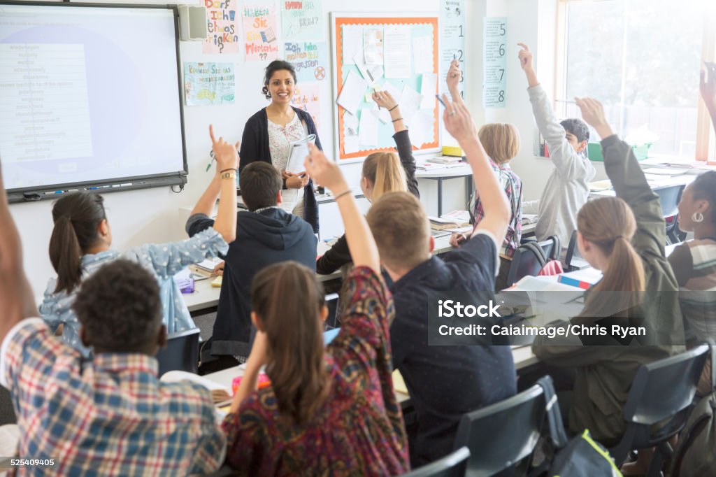 Rear view of teenage students raising hands in classroom  Classroom Stock Photo