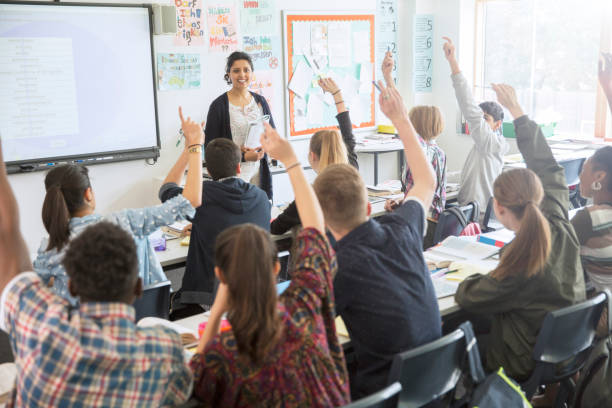 rear view of teenage students raising hands in classroom - 教 個照片及圖片檔