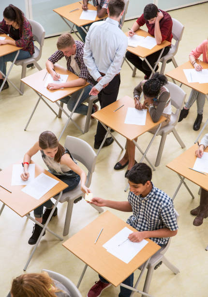 istock Overhead view of students passing note between desks during their GCSE exam 525409563