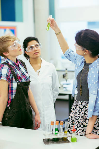 Teacher and students during chemistry lesson, wearing protective eyewear and looking at test tube with green liquid  high school high school student science multi ethnic group stock pictures, royalty-free photos & images