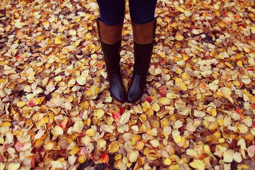 Ready for colder days. Girl in black boots standing on colourful autumn leaves.