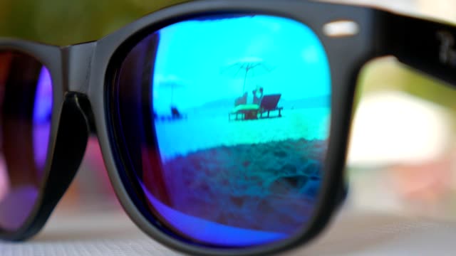 Beach with loungers and parasol reflected in blue mirrored sunglasses